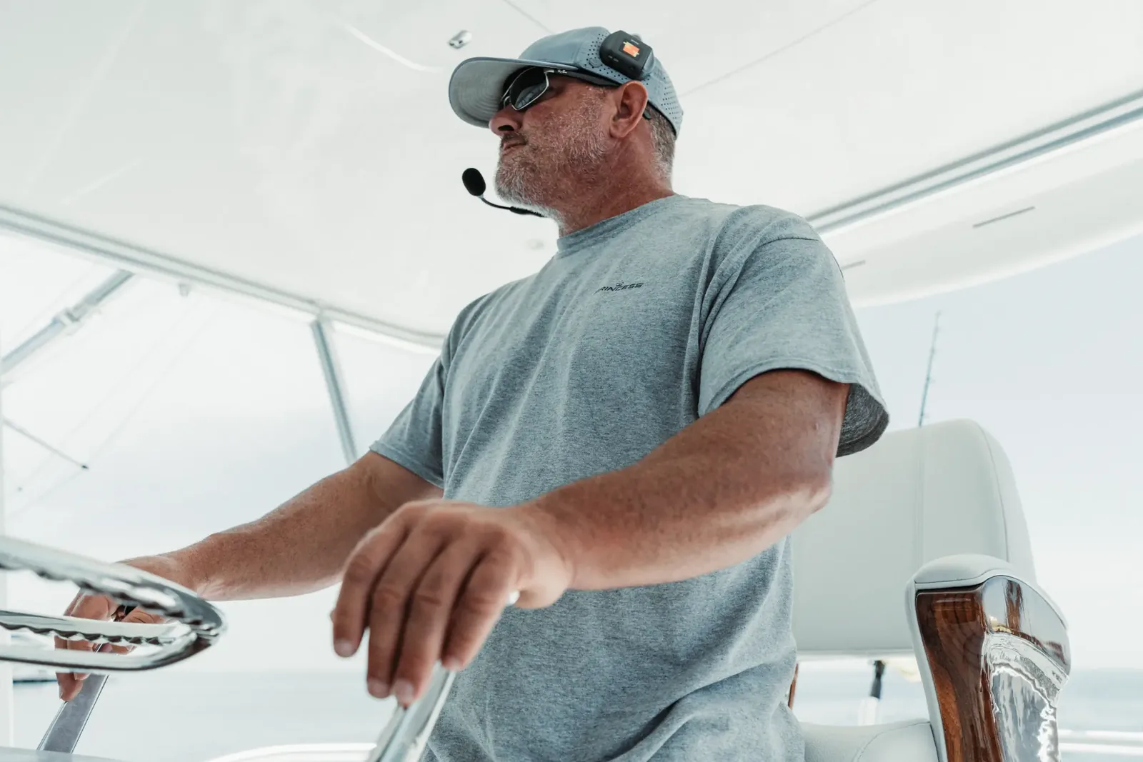 The captain at the wheel of Mjolnir on the flybridge, sunglasses on and a headset over his cap