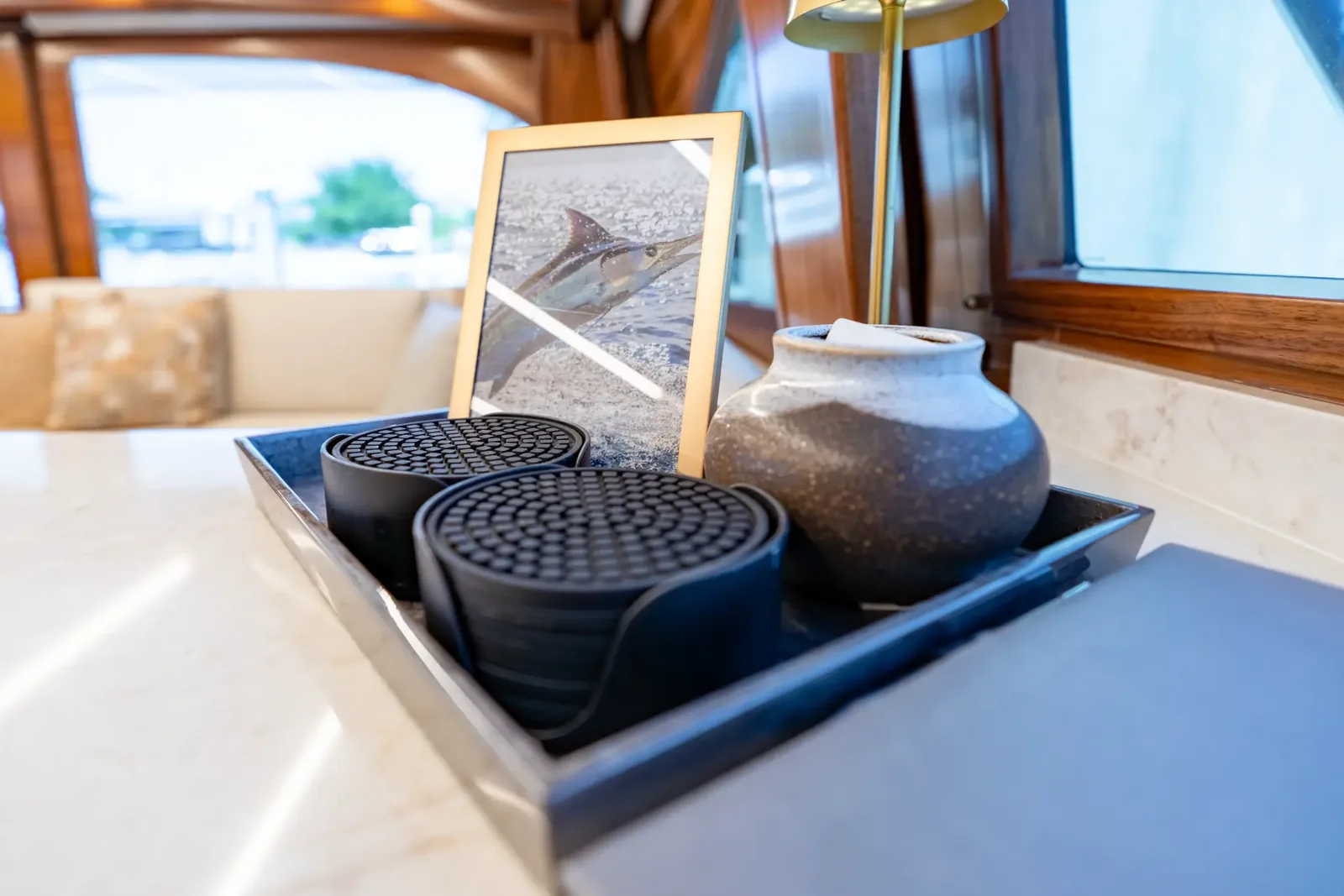 A framed print of a marlin, a stone vase and a tray of coasters on the salon counter, with the windows beyond